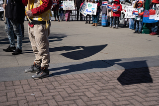 The march is led by four people holding flags: two American flags and two Karen flags.