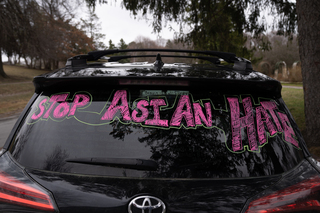 “Stop Asian Hate” is written on the rear windshield of a car parked near the rally.